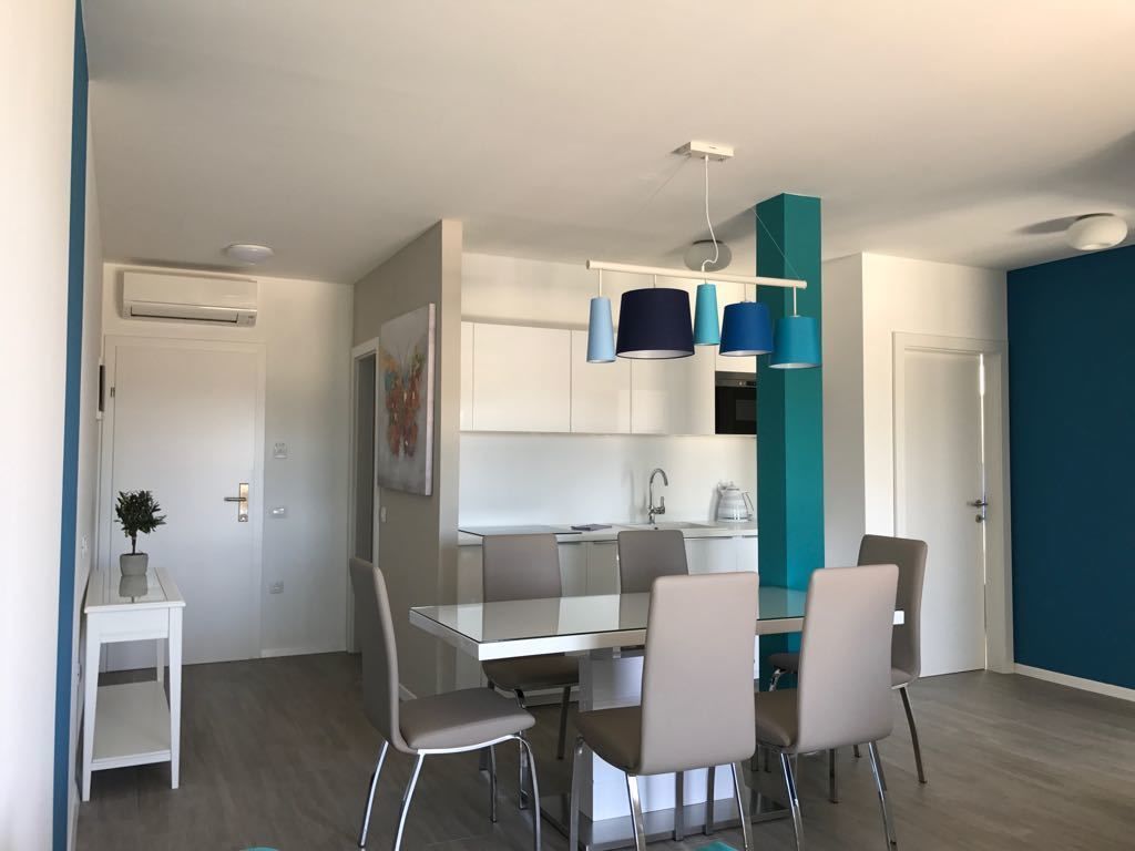 Une cuisine moderne dotée d’un îlot central, de meubles blancs et d’un mur d’accent de couleur turquoise.