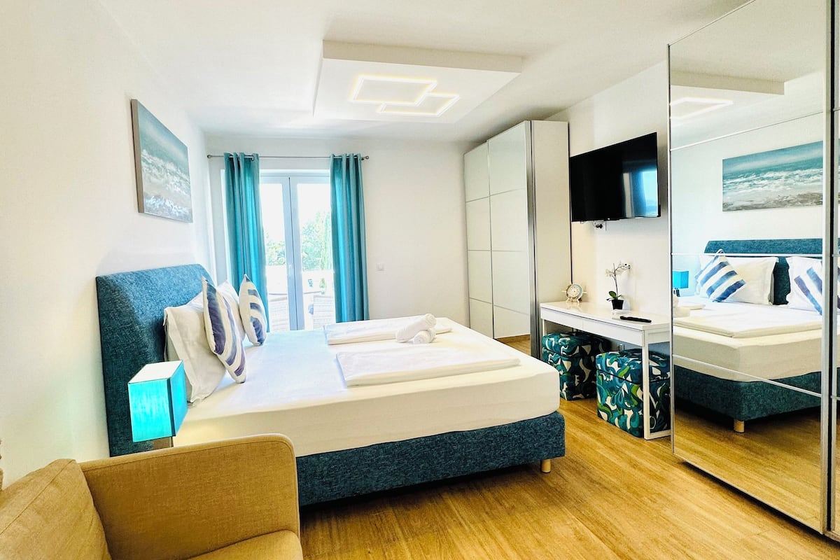 A modern hotel room with a bed, a desk, a chair, and a large mirror.