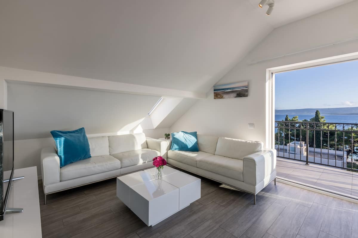A modern living room with a white sofa, a coffee table, and a view of the sea through a balcony.