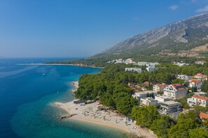 A coastal town with a beach, buildings, and a mountainous backdrop.