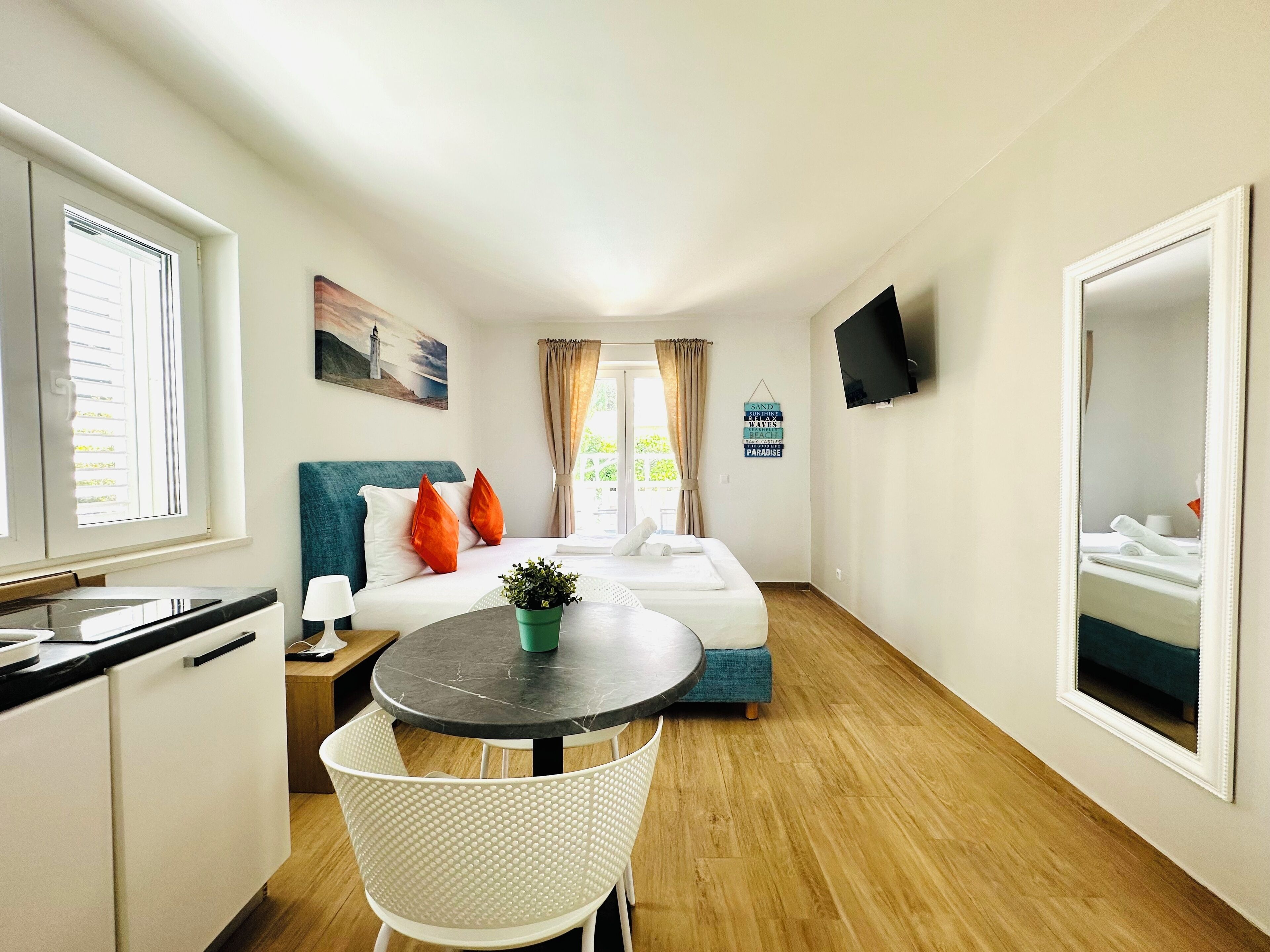 A compact hotel room with a bed, a small dining table, a chair, a TV, and a window with curtains.