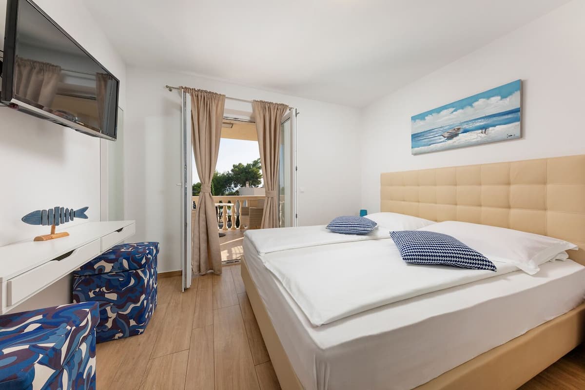 A hotel room with a bed, a TV, a desk, and a balcony with curtains.