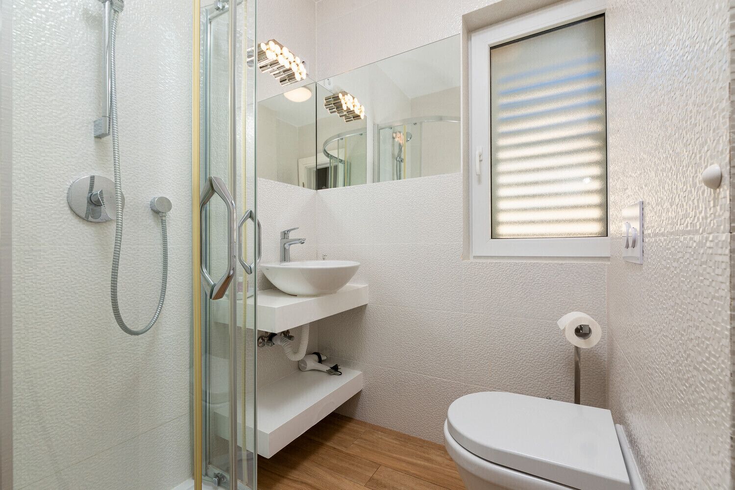 A bathroom with a glass-enclosed shower, a white sink, a mirror, and a toilet.