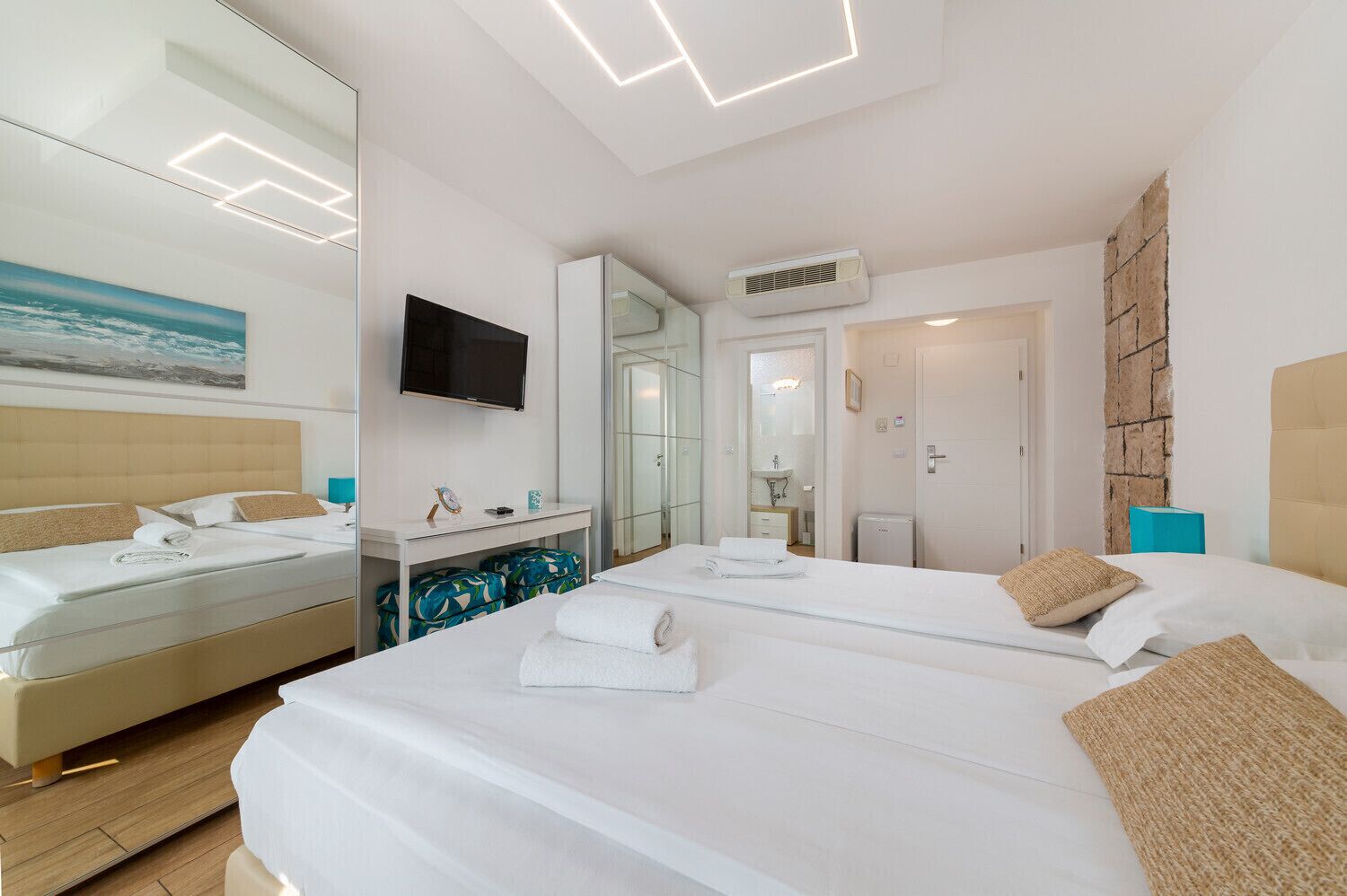A modern hotel room with two beds, a flat-screen TV, a mirror, and a bathroom visible through an open door.