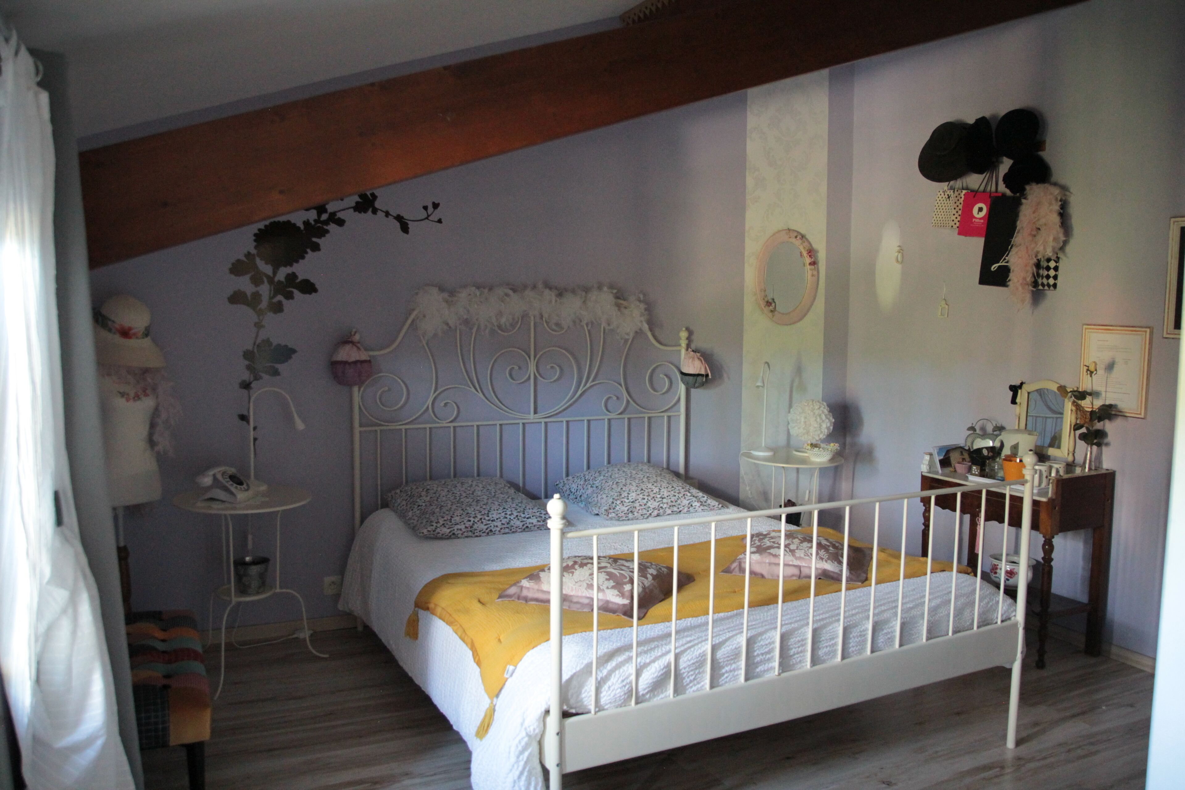 A bedroom with a white metal bed frame, a bedside table, a small chair, and a wall-mounted vanity with a mirror.