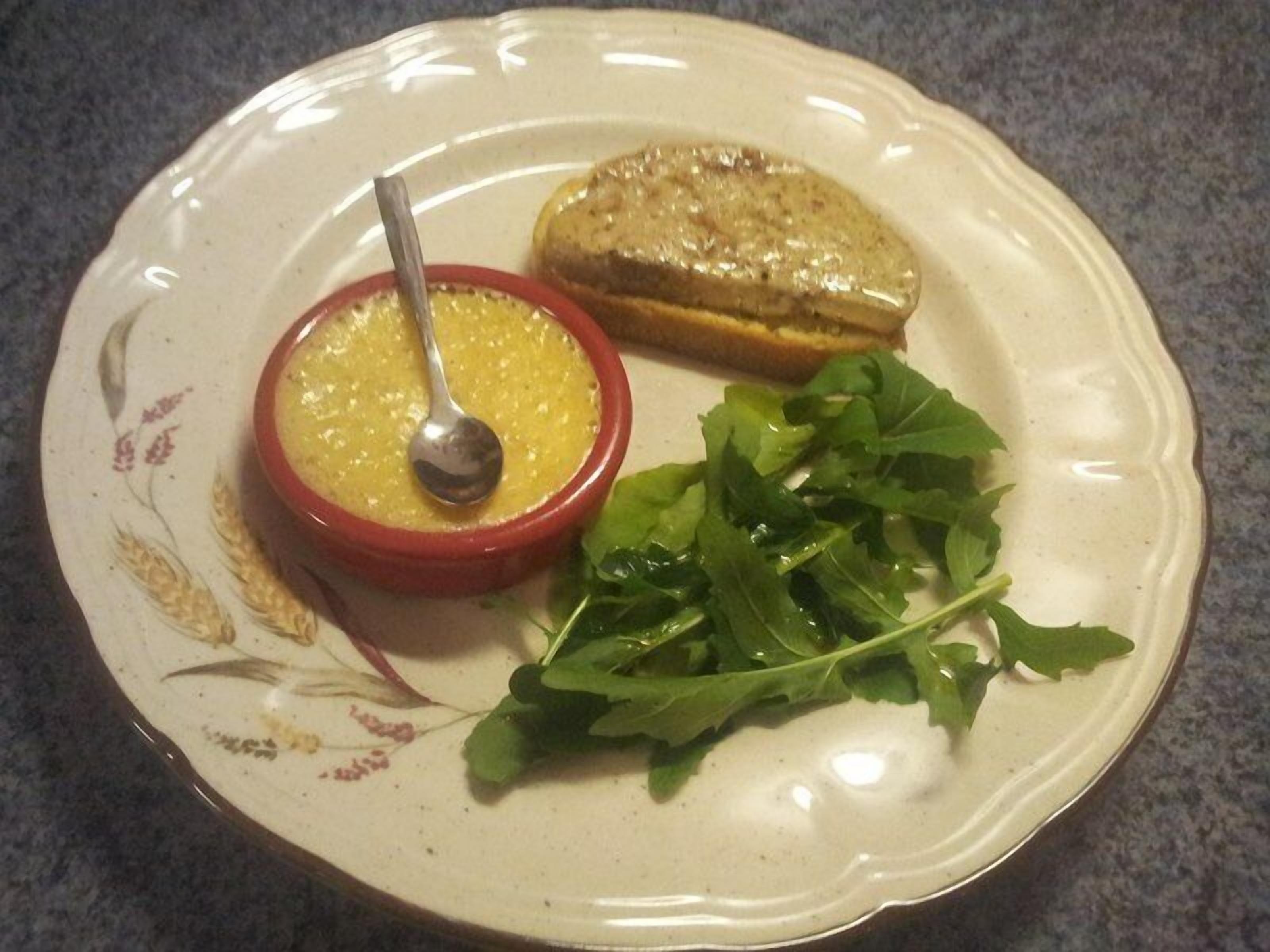 A plate with a bowl of soup, a slice of bread, and some greens.