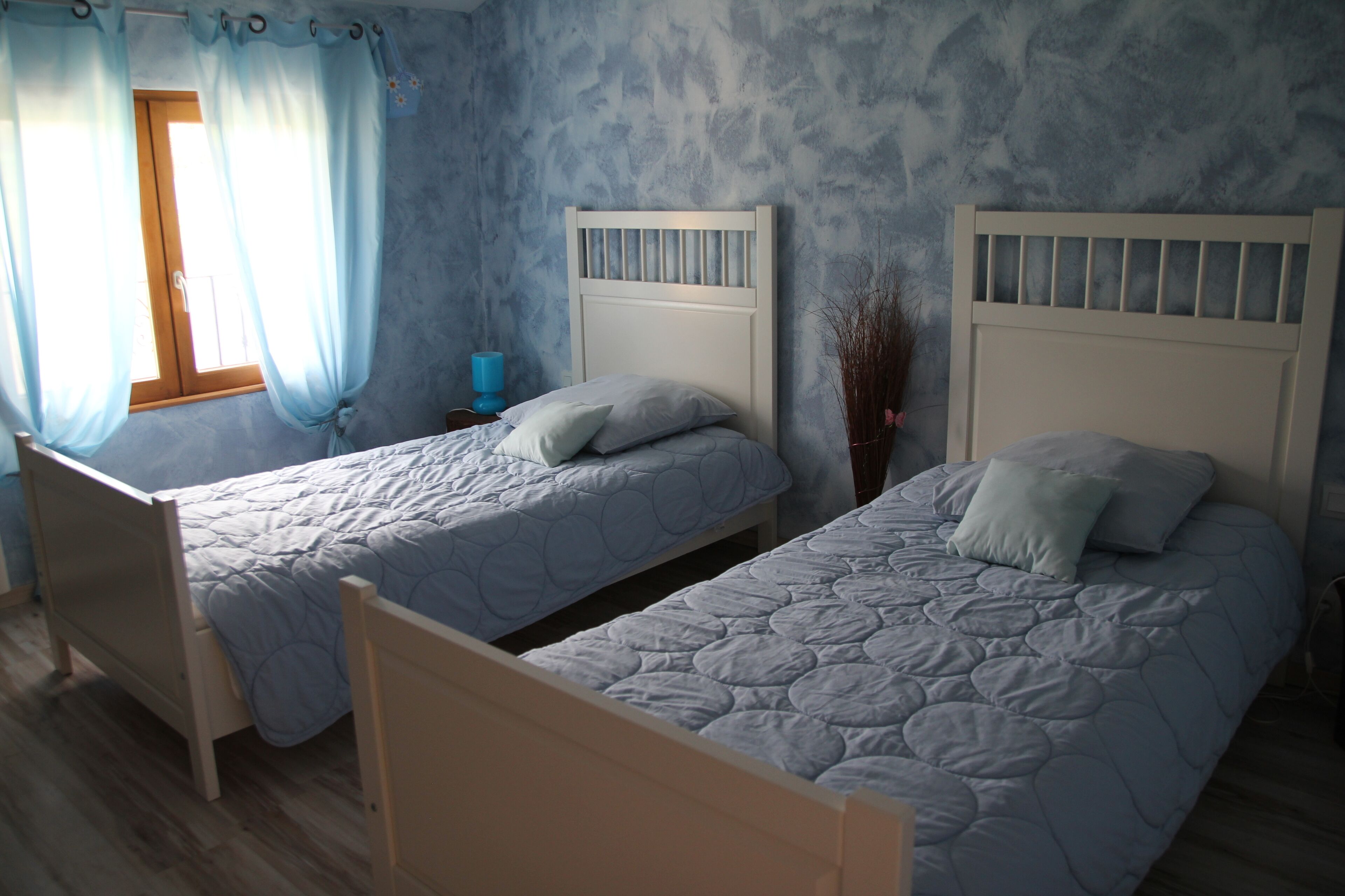 Dos camas individuales con cabeceros, suelo de madera y una ventana con cortinas.