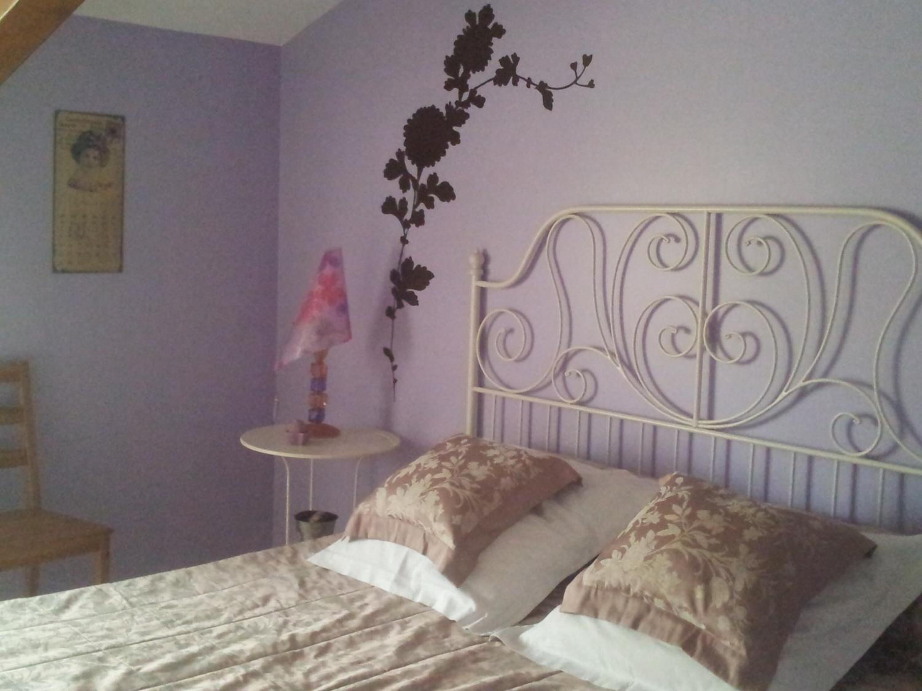 A bedroom with a bed, a nightstand, a lamp, and a decorative wall piece.