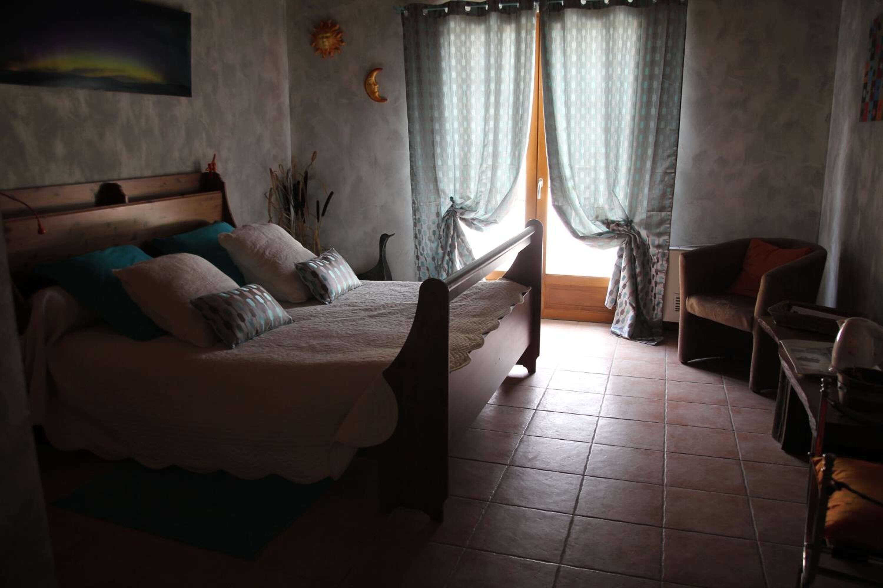A bedroom with a bed, a chair, a table, and a window with curtains.