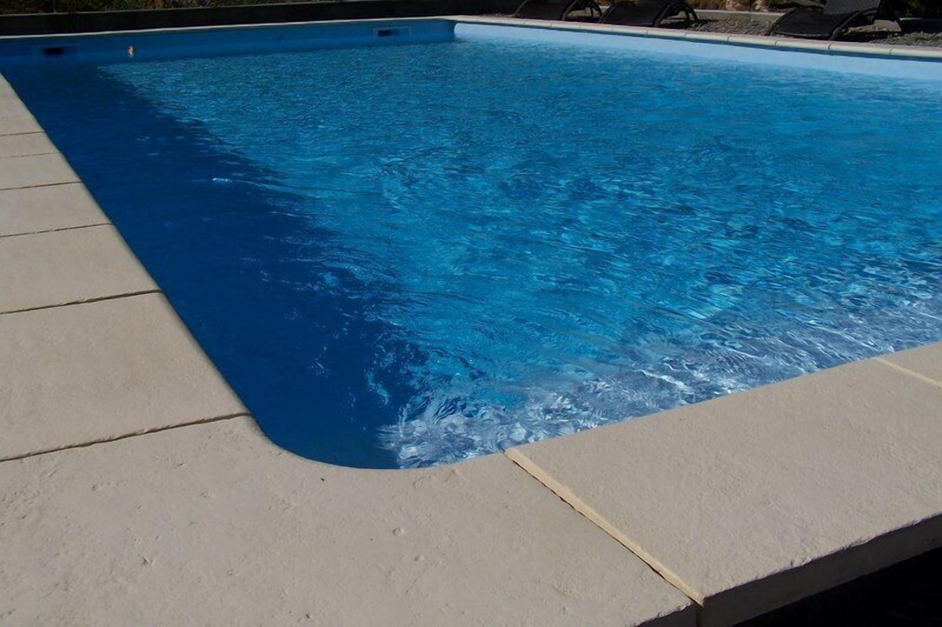 Une piscine rectangulaire à l’eau d’un bleu limpide, entourée d’une terrasse aux couleurs claires.