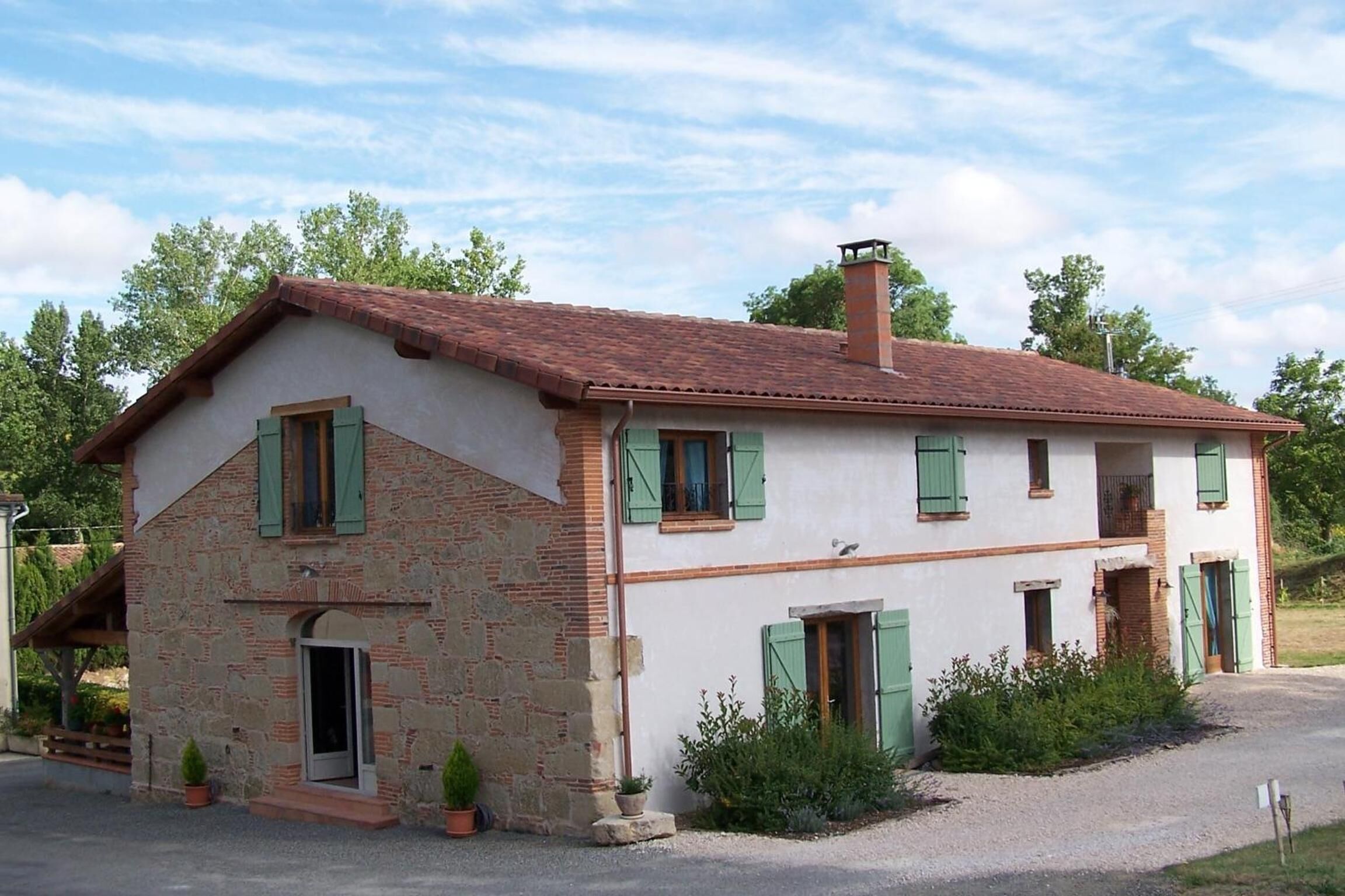 A two-story house with a sloped roof, green shutters, and a chimney.