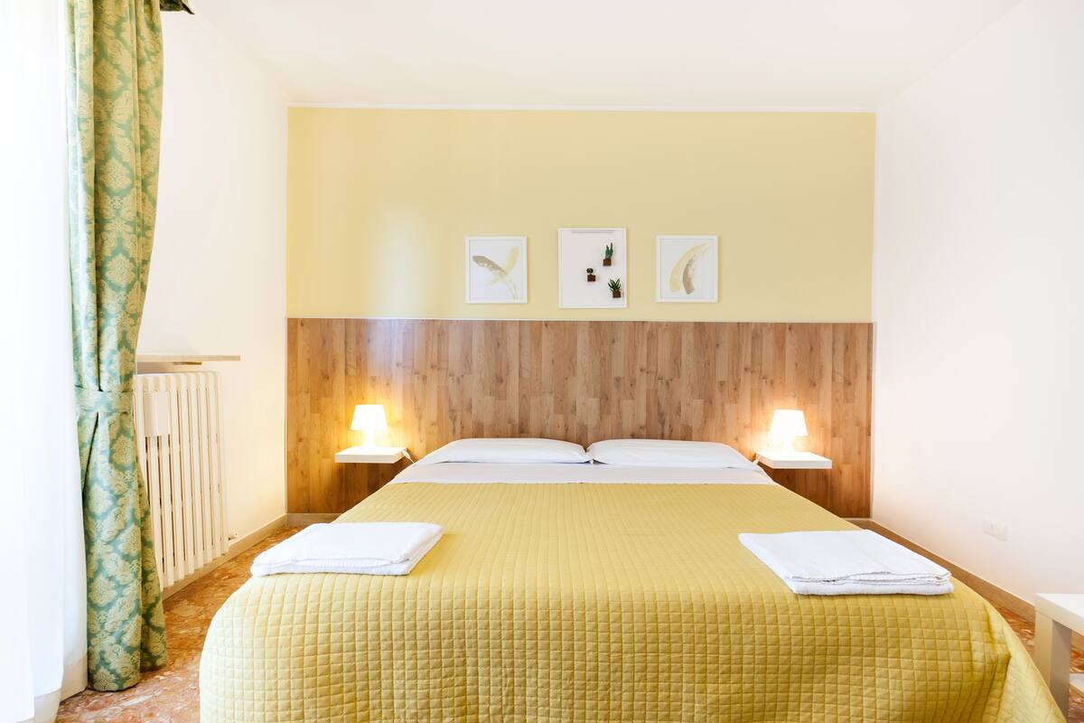 Een hotelkamer met een groot bed, twee nachtkastjes met lampen, een houten hoofdeinde en drie ingelijste foto's aan de muur.