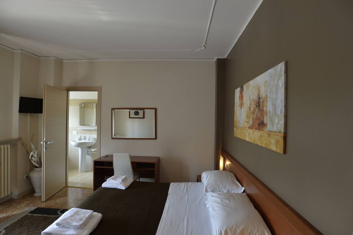 Een hotelkamer met een bed, een bureau, een stoel, een televisie en een badkamer zichtbaar door een open deur.