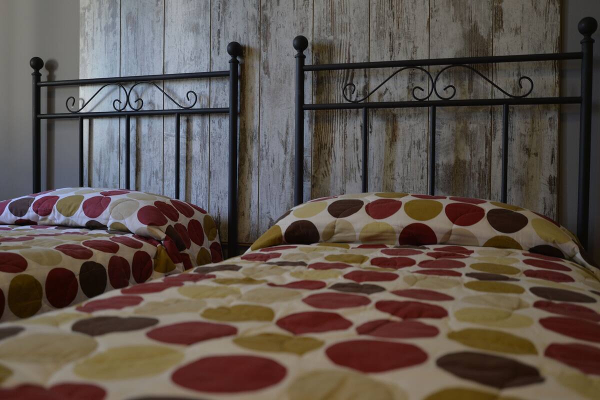 Een bed met een stippenbedekking en een metalen hoofdbord tegen een houten wand.