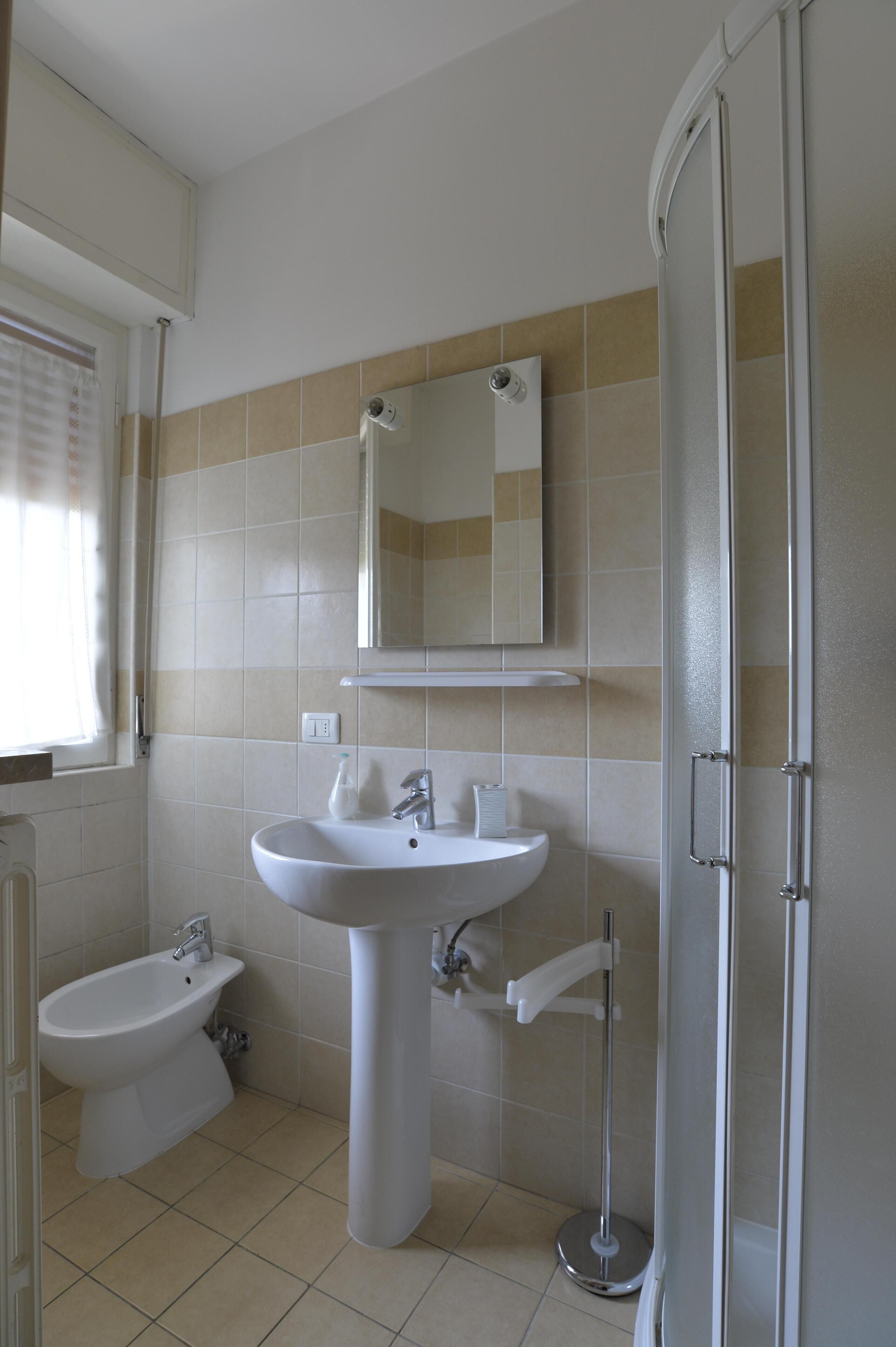 A bathroom with a pedestal sink, a bidet, a mirror, and a shower enclosure.