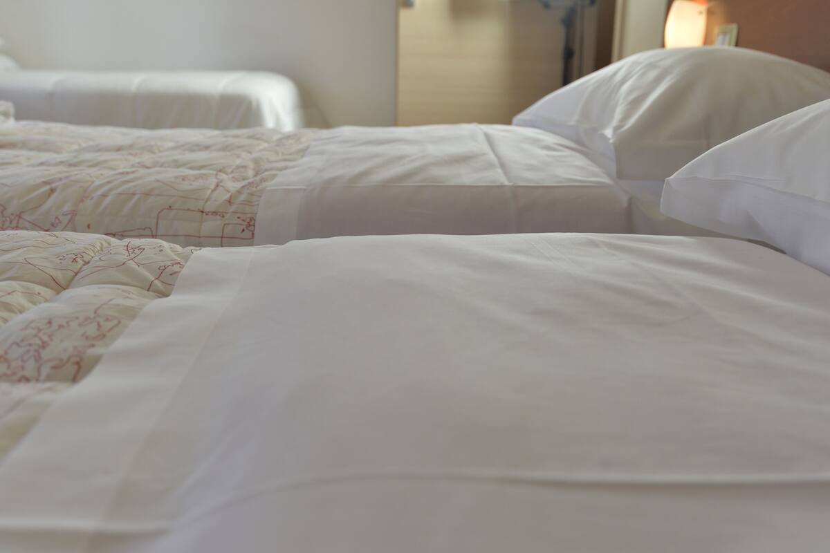 Een hotelkamer met twee bedden, elk voorzien van witte lakens en een deken met bloemenprint.