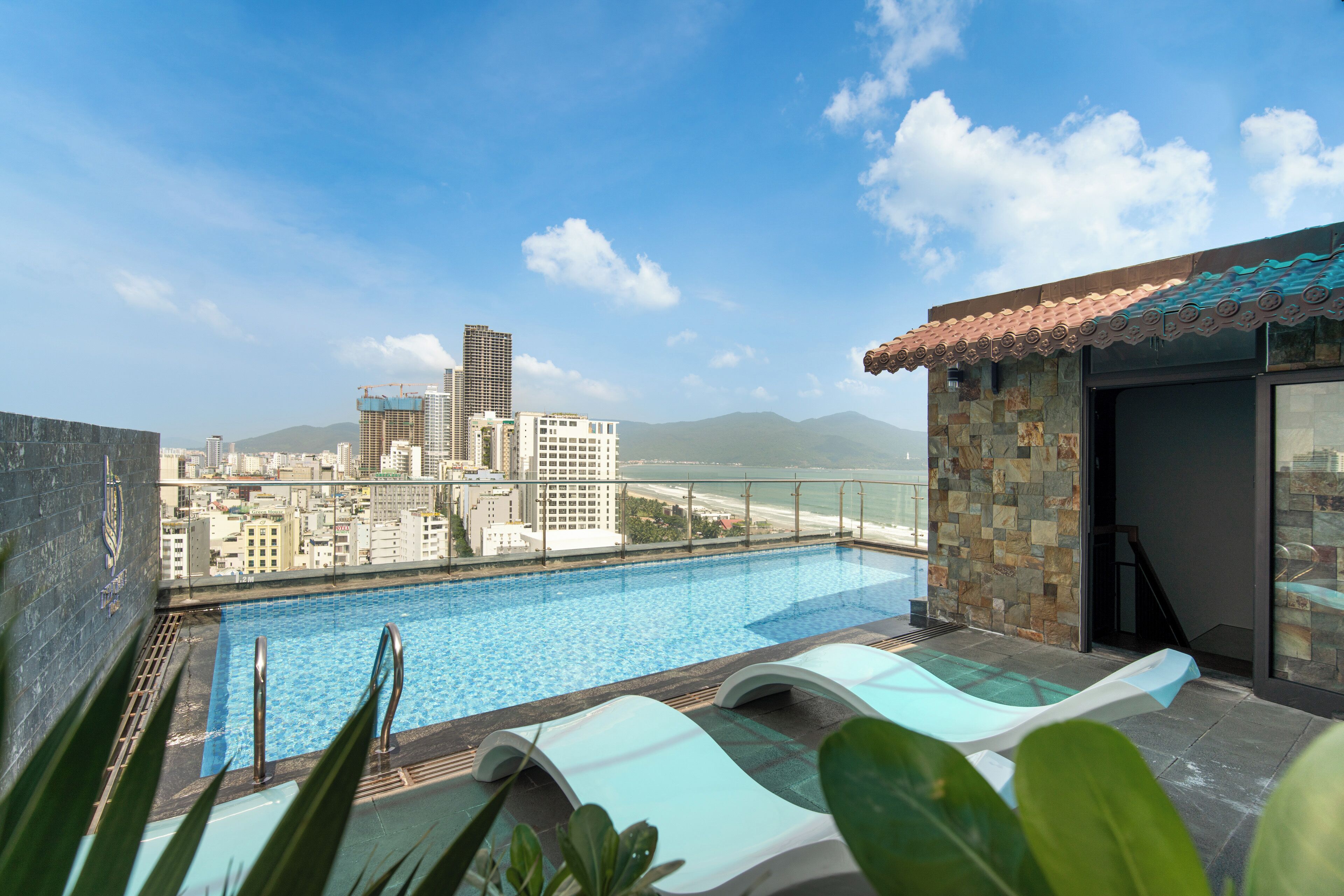 A rooftop pool with a city view, including a tall building and mountains in the distance.