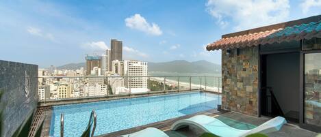 Una piscina en la azotea con vistas a la ciudad, incluyendo un edificio alto y montañas al fondo.
