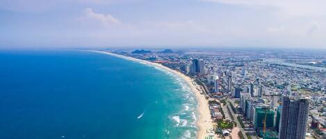 Vista aérea de uma cidade costeira com uma extensa praia, edifícios altos e um oceano azul límpido.