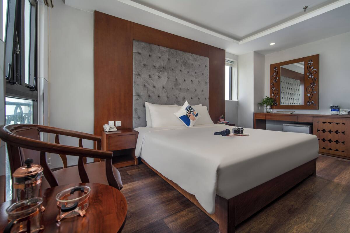 A hotel room with a large bed, wooden headboard, a wooden desk, and a mirror.