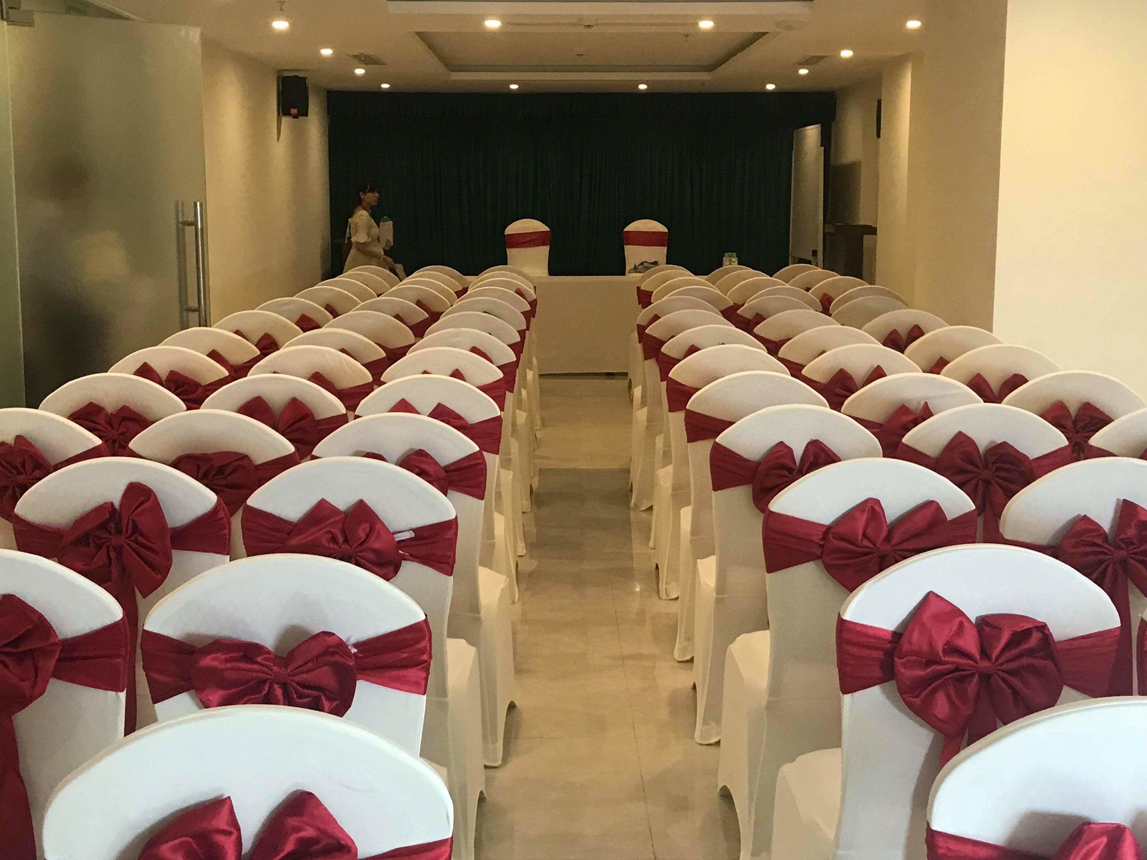 A conference room with rows of white chairs, each adorned with a red bow.