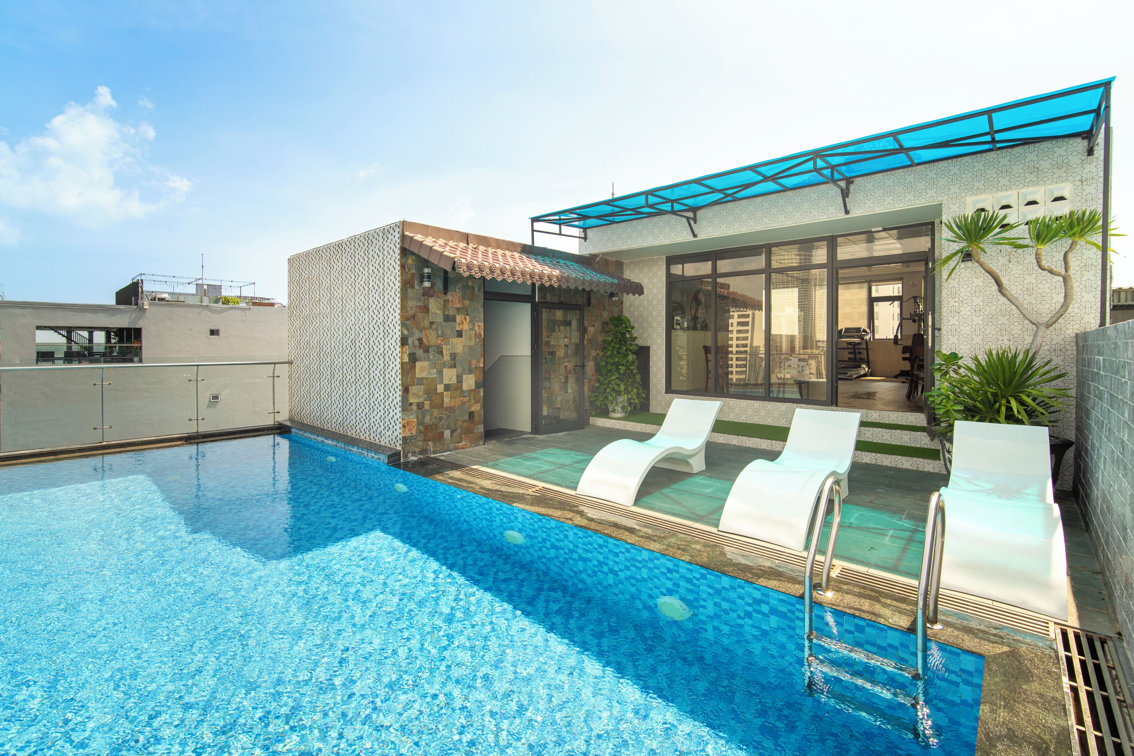 A rooftop swimming pool with a glass enclosure, lounge chairs, and a small garden area.