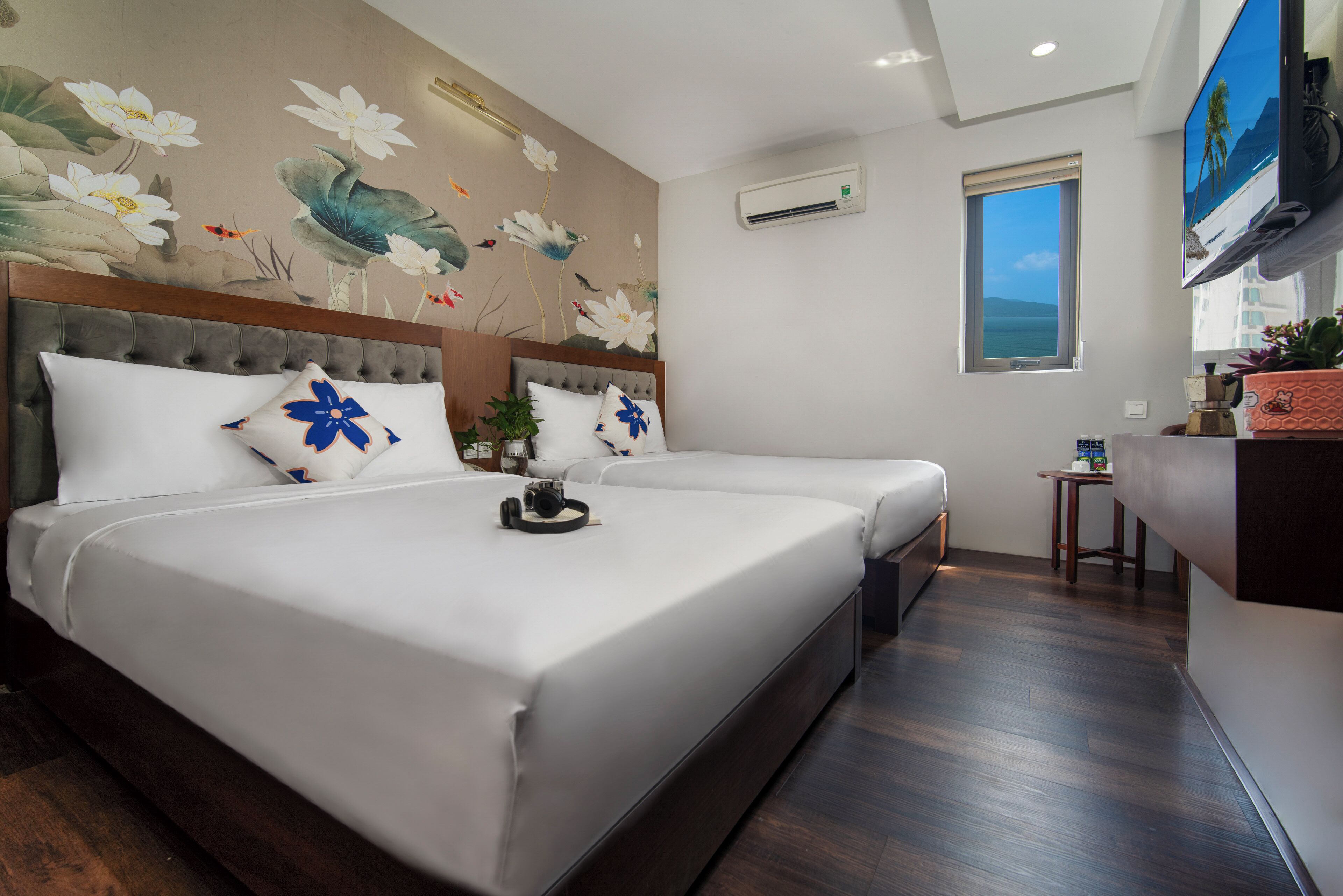 Quarto de hotel com duas camas, televisão, ar condicionado, janela com vista e um mural decorativo na parede.