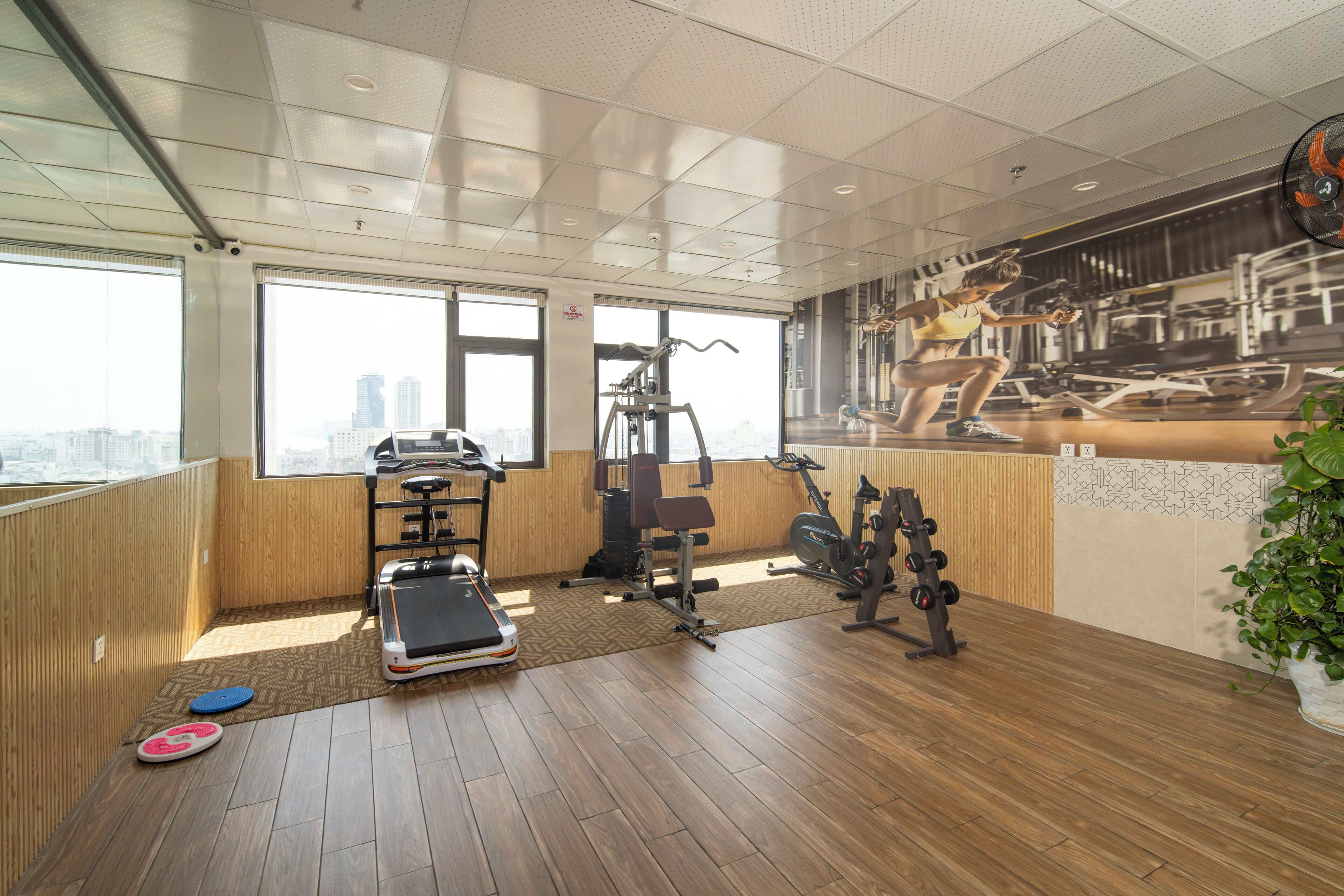 Un gimnasio con equipo de ejercicio, amplias ventanas y vistas a la ciudad.