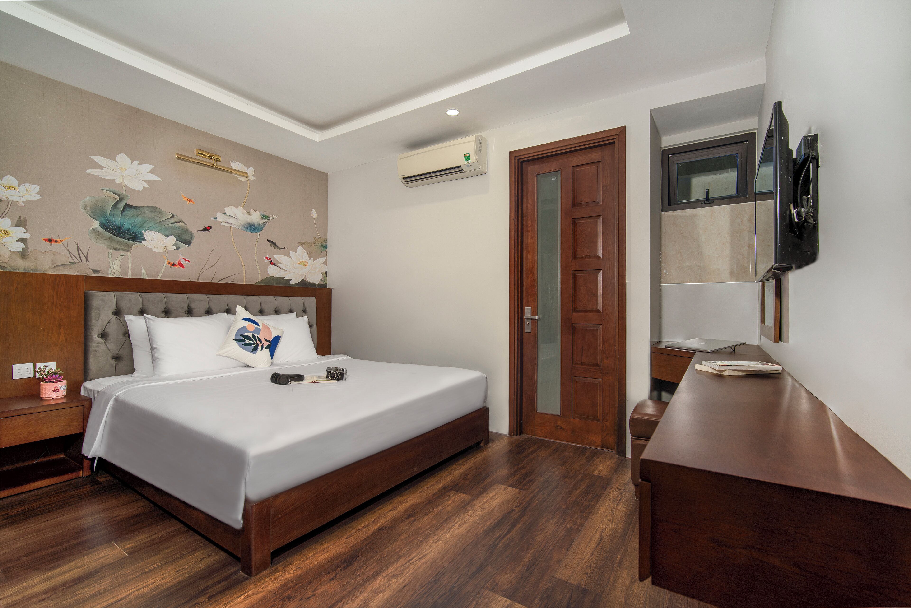 A bedroom with a bed, wooden headboard, a wall-mounted TV, and a wooden desk.