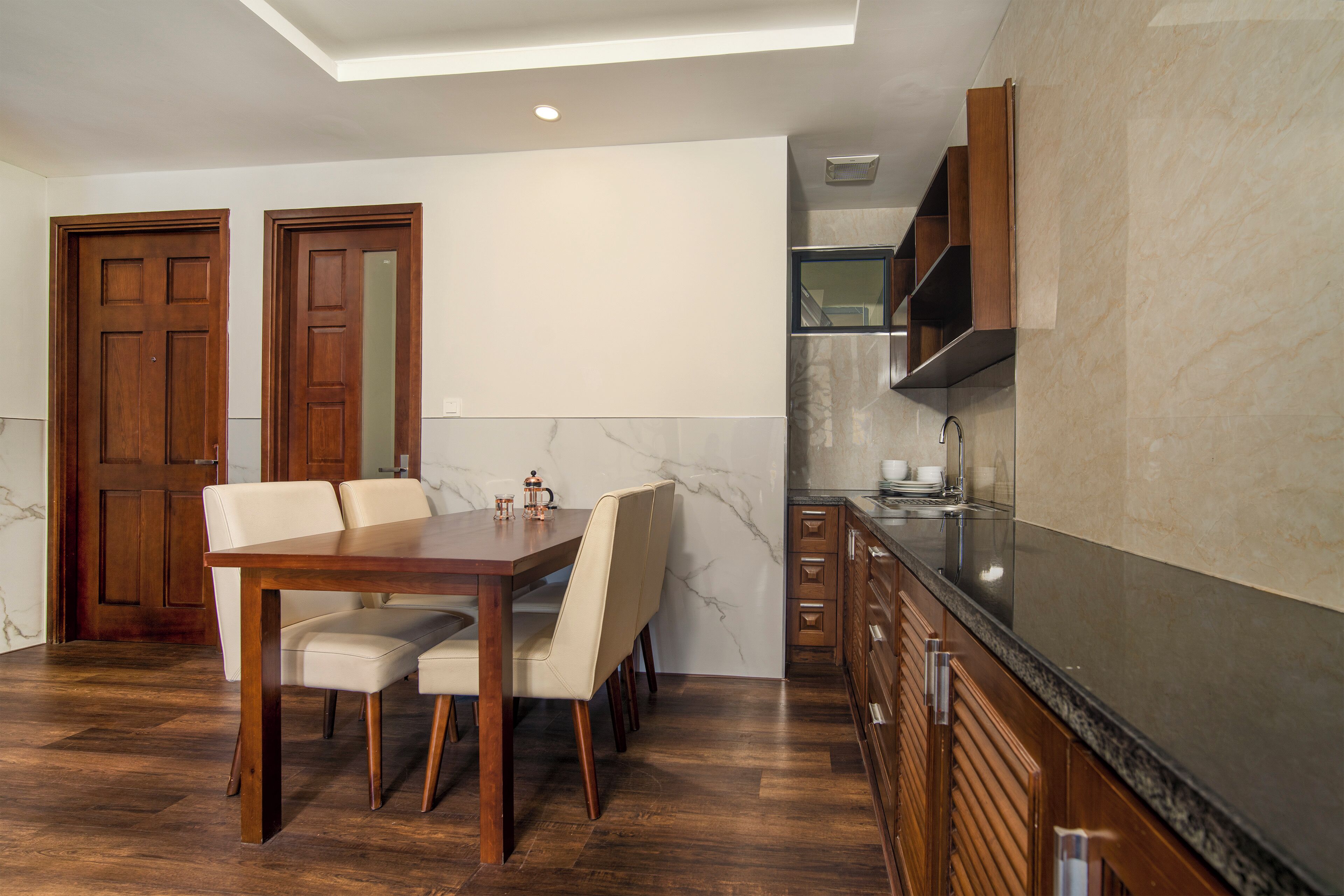 Une cuisine moderne dotée d’un plan de travail en marbre, de meubles en bois et d’un coin repas avec une table et des chaises en bois.