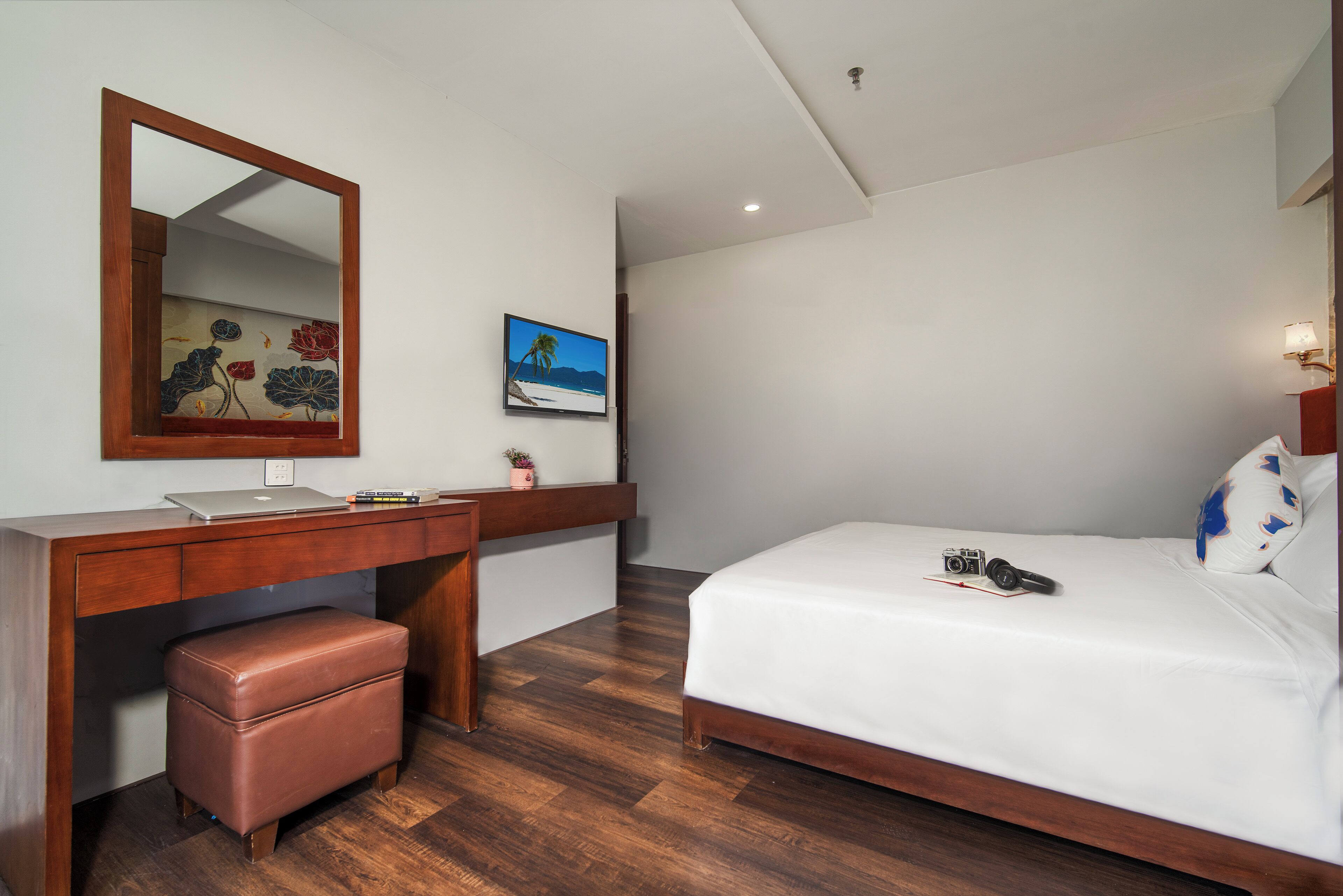 Un dormitorio con un escritorio de madera, un espejo, una cama y una mesita de noche.
