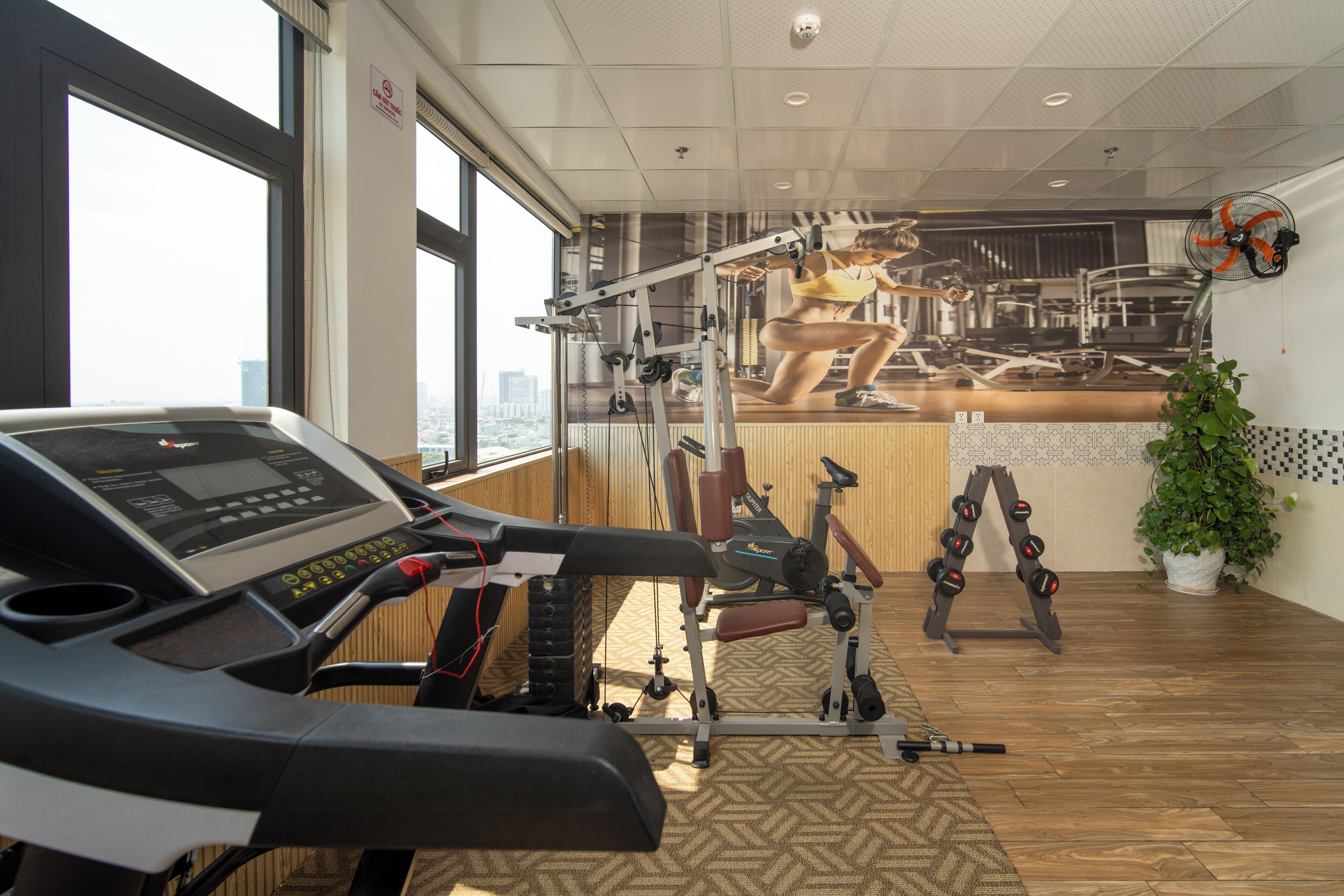 A gym with a treadmill, weight machines, and a large window offering a city view.
