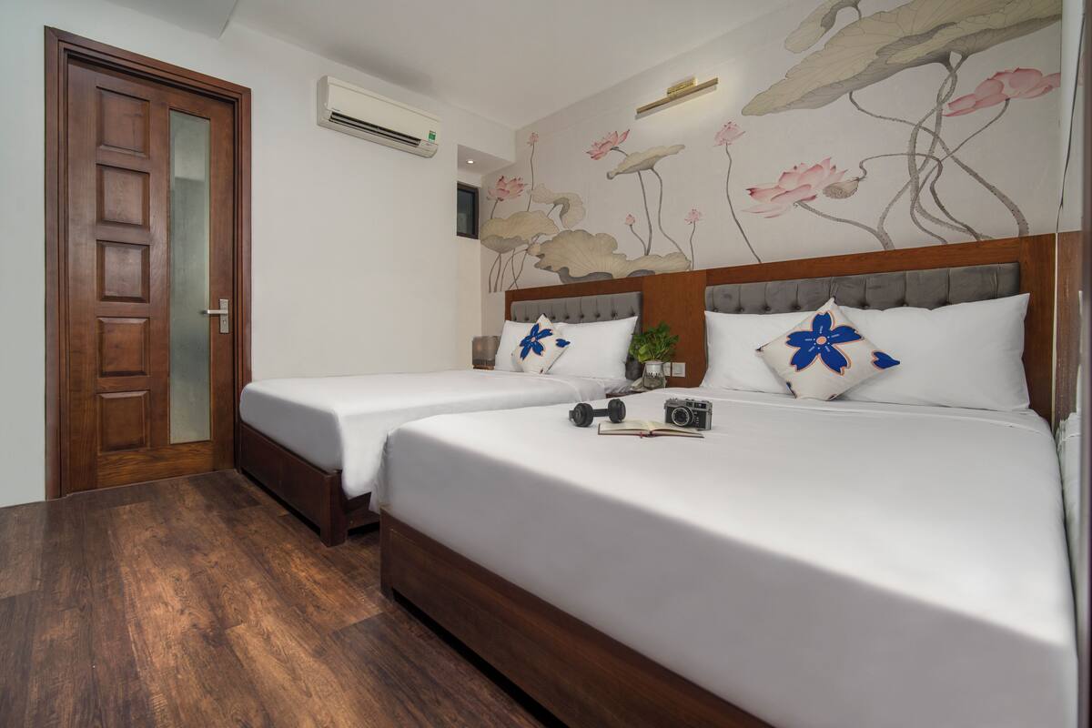 A hotel room with two single beds, a wooden door, a wall-mounted air conditioner, and a floral mural.