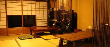 Um quarto japonês tradicional com tatames, uma mesa de madeira baixa, almofadas e portas deslizantes.