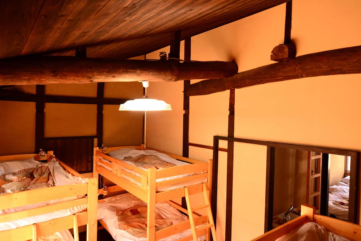 A rustic wooden room with bunk beds, a single bed, and a mirror reflecting the room.