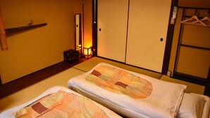 Una habitación japonesa tradicional con suelo de tatami, dos esteras de tatami, una puerta corredera shoji, un perchero y una mesita de noche con lámpara.