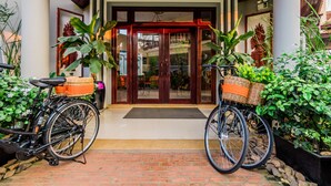 A hotel entrance with a brick pathway leading to a wooden door. Two bicycles with baskets are parked on either side. - Wheel Garden Residence (Siem Reap)