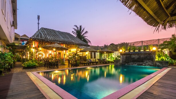 A swimming pool with a wooden deck, a thatched-roof building, and outdoor seating. - Wheel Garden Residence (Siem Reap)