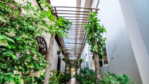 A narrow corridor with a wooden pergola overhead, surrounded by lush greenery and potted plants. - Wheel Garden Residence (Siem Reap)