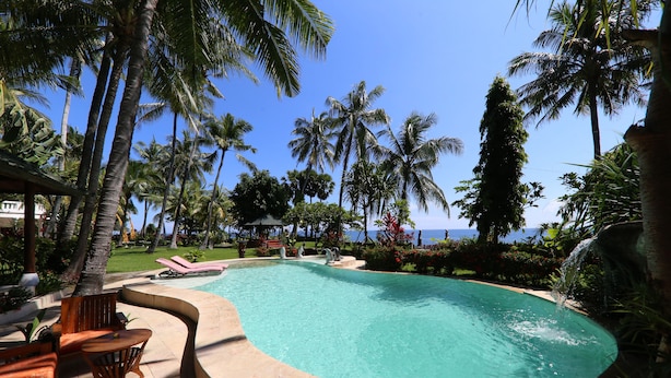 A pool with a curved edge, surrounded by palm trees and lounge chairs. - Felicianas Resort (Tejakula)