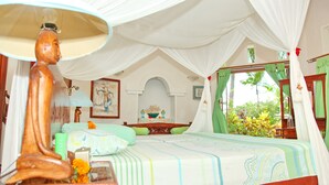 A room with a bed, a wooden nightstand, a lamp, and a view of greenery outside. - Felicianas Resort (Tejakula)