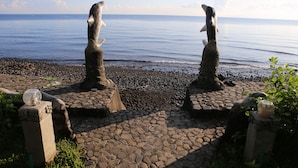 A stone pathway leading to a beach with two stone figures, a clear sky, and calm sea. - Felicianas Resort (Tejakula)