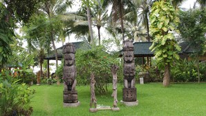 A garden with stone statues, a 'Welcome' sign, and a traditional building with a green roof. - Felicianas Resort (Tejakula)