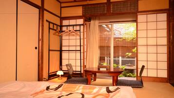 A traditional Japanese room with tatami flooring, a low table with a cushion, a hanging coat rack, and a sliding door leading to a garden.
