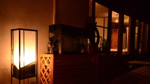 Un espacio al aire libre tenuemente iluminado, con un banco de madera y una silla de metal.