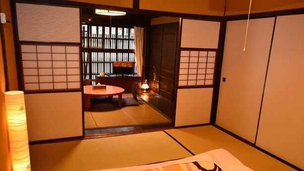 Una habitación japonesa tradicional con suelo de tatami, una mesa baja con cojines y puertas correderas.