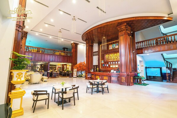 A spacious lobby with a high ceiling, wooden columns, and a staircase leading to an upper level.