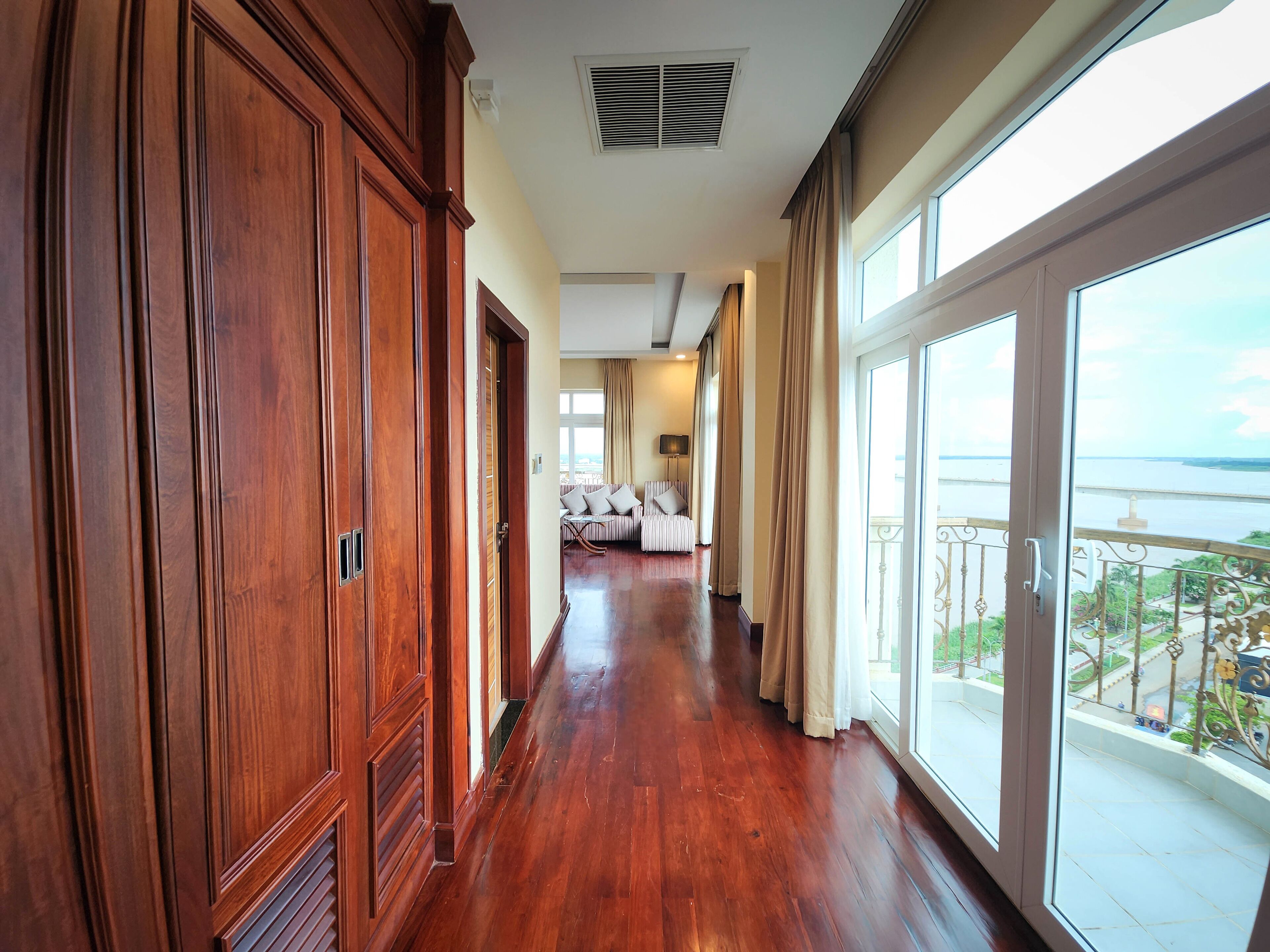 A hotel corridor with wooden paneling, a balcony with a view of the sea, and a seating area with a sofa and chairs.