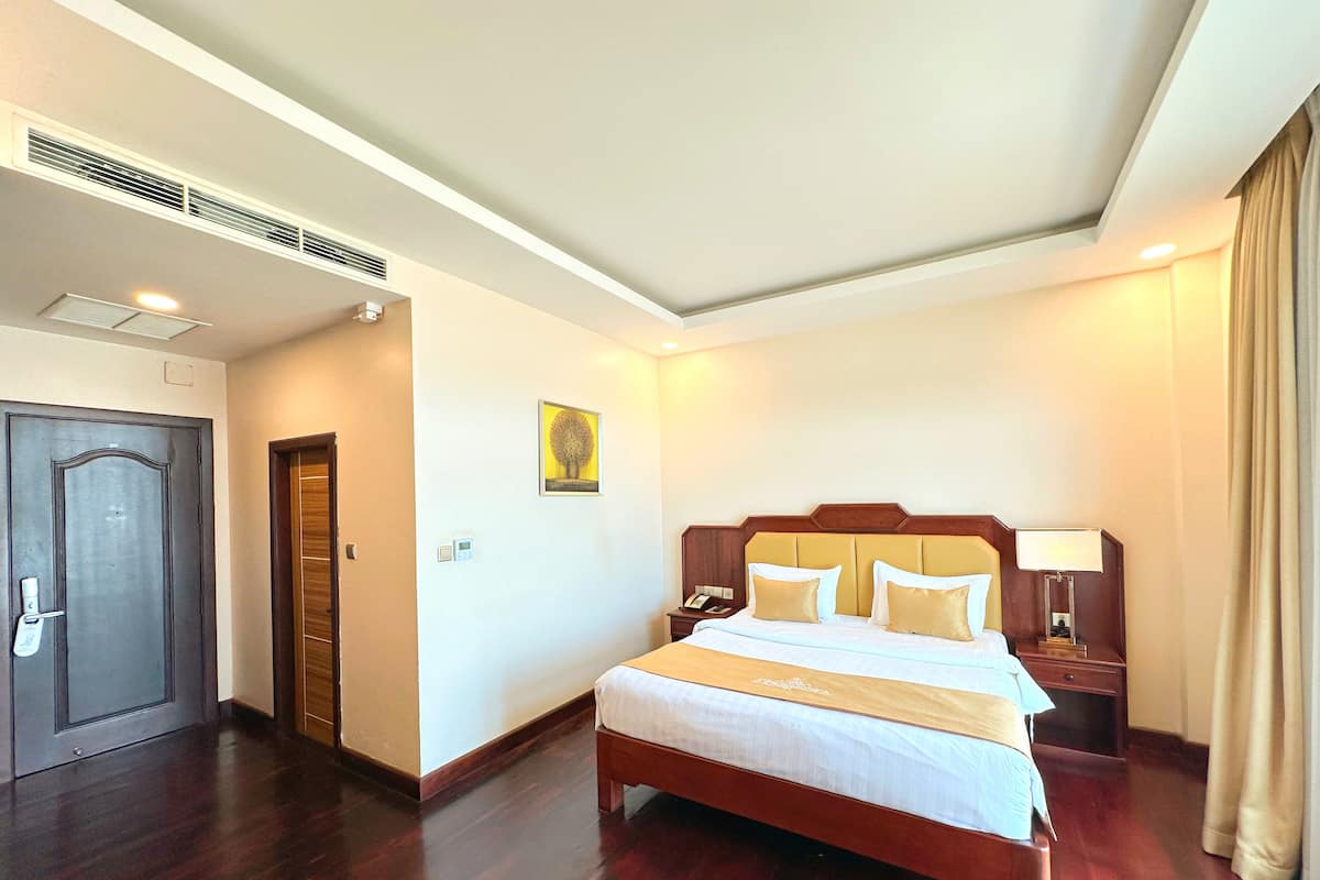 Une chambre d’hôtel avec un grand lit, une table de chevet avec une lampe, une porte et une bouche d’aération fixée au mur.