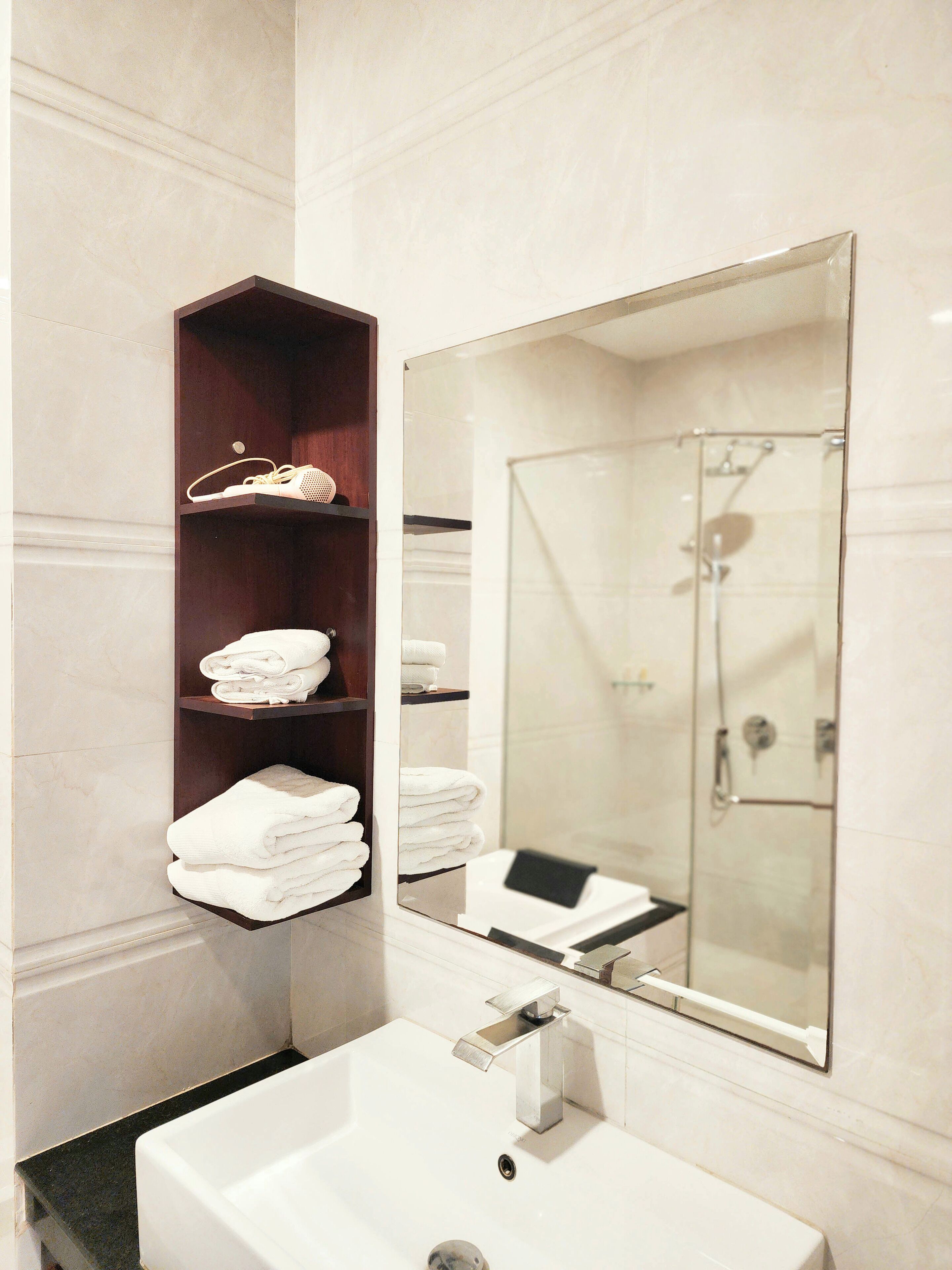 A modern bathroom with a large mirror, a white sink, and shelves holding towels and a pair of shoes.